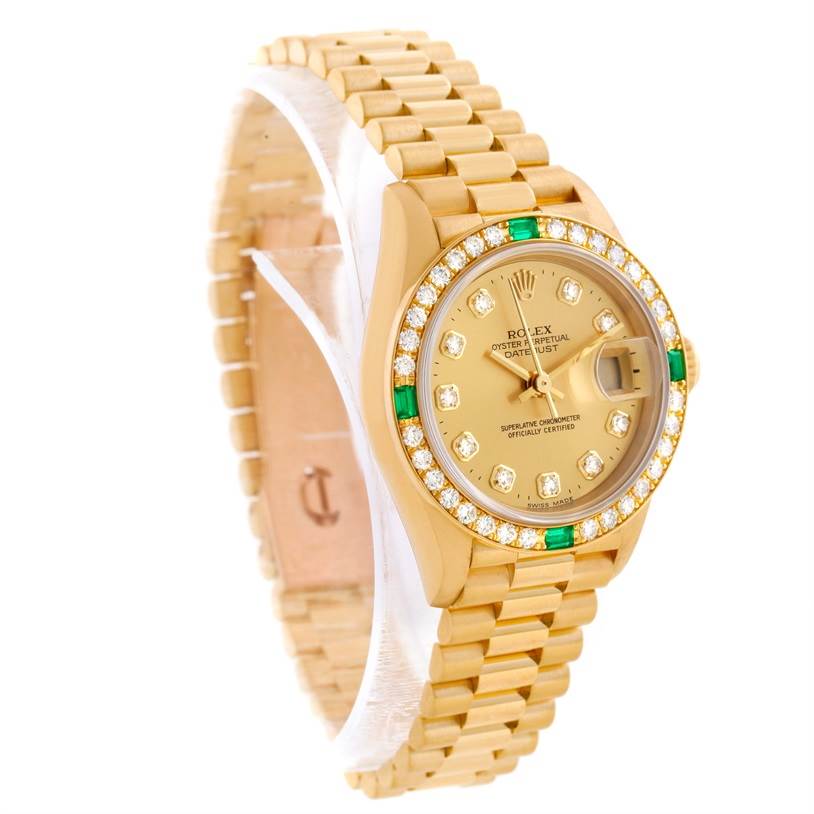 This image shows a Rolex President 69078 Women's Yellow Gold Champagne Dial 69078 Women's Yellow Gold Champagne Dial model watch with a gold dial, diamond and emerald bezel, and a gold bracelet, viewed from an angled perspective.