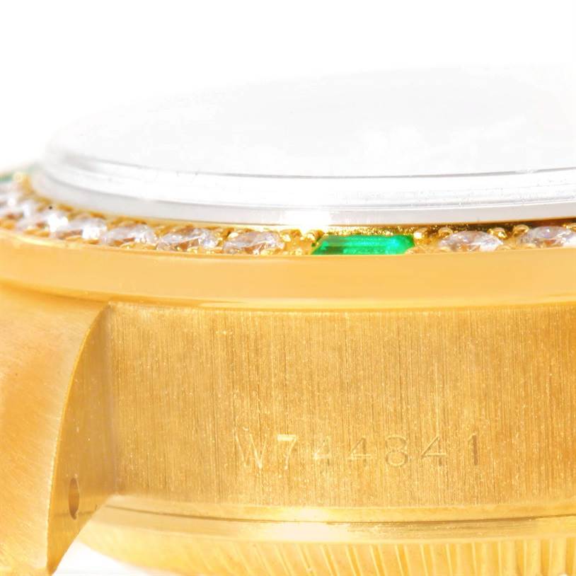 This close-up shot of a Rolex President 69078 Women's Yellow Gold Champagne Dial 69078 Women's Yellow Gold Champagne Dial watch shows the side of the case, bezel with diamonds and emeralds, and a part of its serial number.