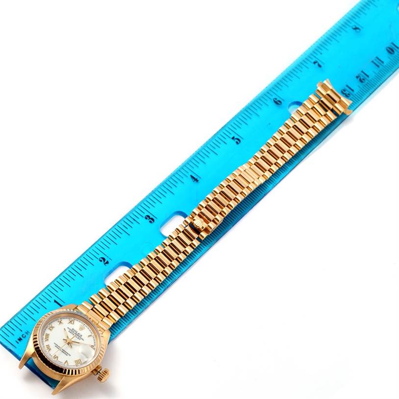 The image shows a President model Rolex watch laid flat beside a blue ruler for size reference.
