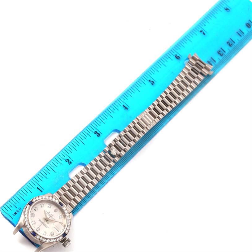 The Rolex President 79179 Women's White Gold Silver Dial 79179 Women's White Gold Silver Dial model watch is shown laying flat next to a ruler, displaying the face and the metal band.