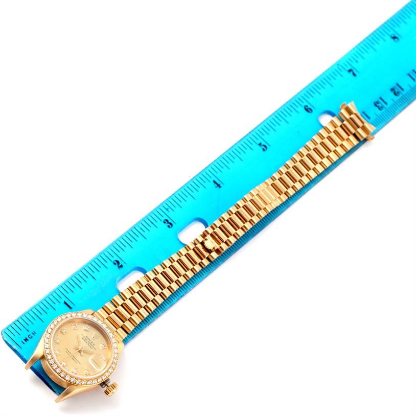 The Rolex President 69168 Women's Yellow Gold Champagne Dial 69168 Women's Yellow Gold Champagne Dial model watch is shown laid flat alongside a blue ruler, displaying the watch face and entire band.
