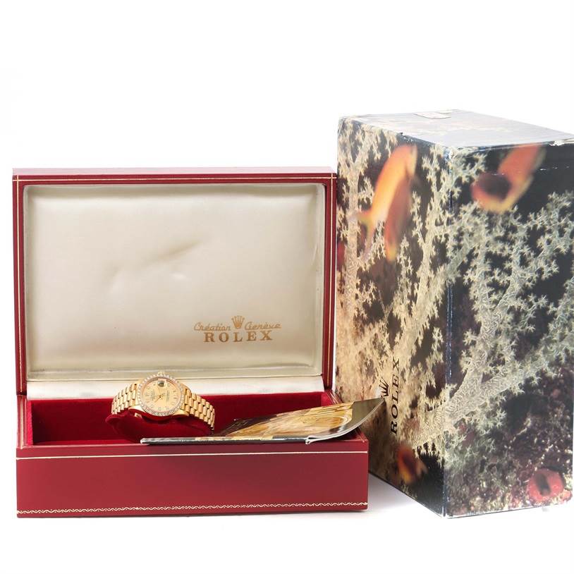 The image shows a Rolex President 69168 Women's Yellow Gold Champagne Dial 69168 Women's Yellow Gold Champagne Dial watch in a red box with the lid open and an outer decorative box.