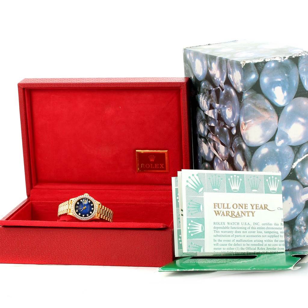 The image shows a Rolex President 69138 Women's Yellow Gold Blue Dial 69138 Women's Yellow Gold Blue Dial model watch in a red box, positioned next to warranty cards and packaging.
