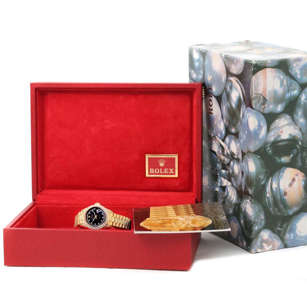 The image shows a Rolex President 69238 Women
s Yellow Gold Black Dial 69238 Women
s Yellow Gold Black Dial model watch in a red case with a booklet, along with its decorative outer box nearby.