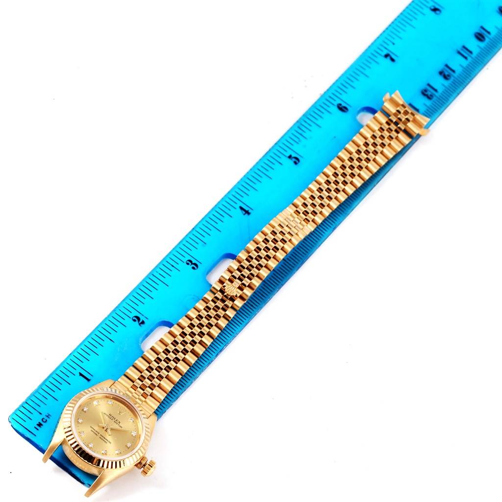 The image shows a Rolex President 76198 Women's Yellow Gold Champagne Dial 76198 Women's Yellow Gold Champagne Dial model watch laid next to a blue ruler, highlighting its face and bracelet length.