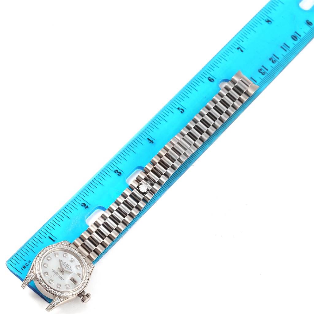 The image shows a President model Rolex watch, with its face and bracelet laid out next to a blue ruler for measurement.