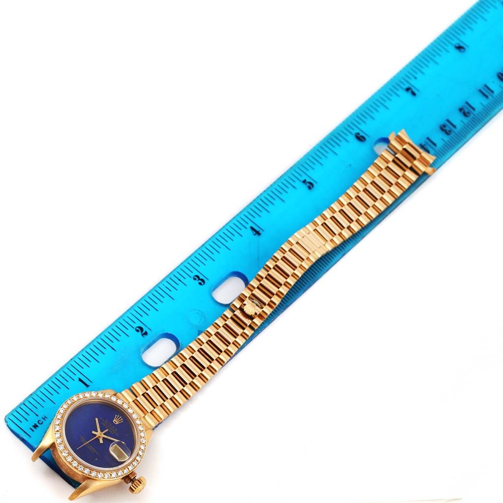 This image shows a Rolex President 69178 Women's Yellow Gold Blue Dial 69178 Women's Yellow Gold Blue Dial model watch laid flat next to a blue ruler, displaying the watch case and band.