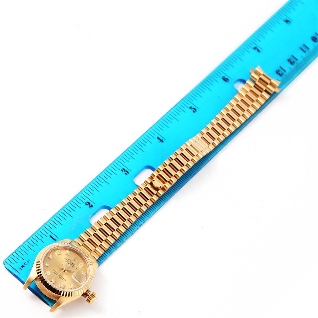 The image shows a Rolex President 69178 Women's Yellow Gold Champagne Dial 69178 Women's Yellow Gold Champagne Dial watch placed next to a blue ruler, displaying the watch face and part of the gold band.