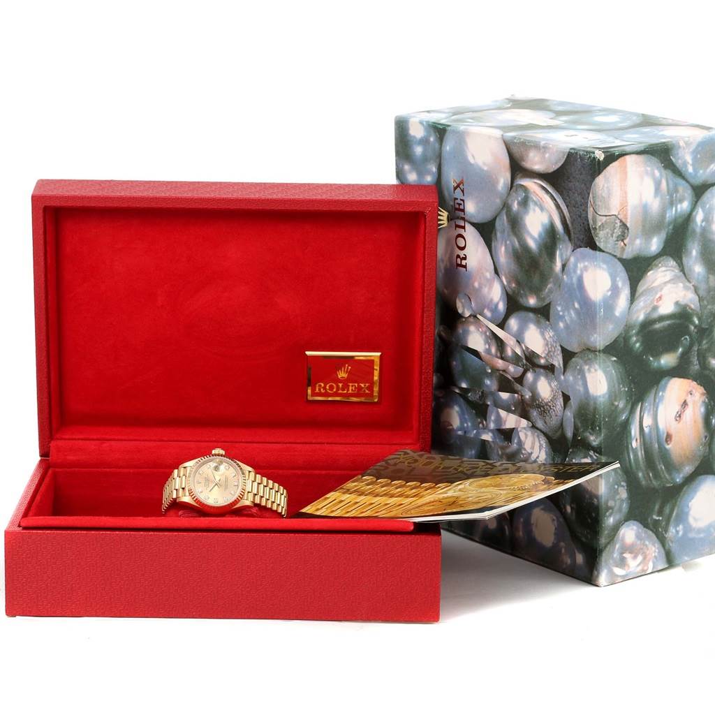 The image shows a Rolex President 69178 Women's Yellow Gold Champagne Dial 69178 Women's Yellow Gold Champagne Dial model watch in its open red case, with packaging and paperwork beside it.