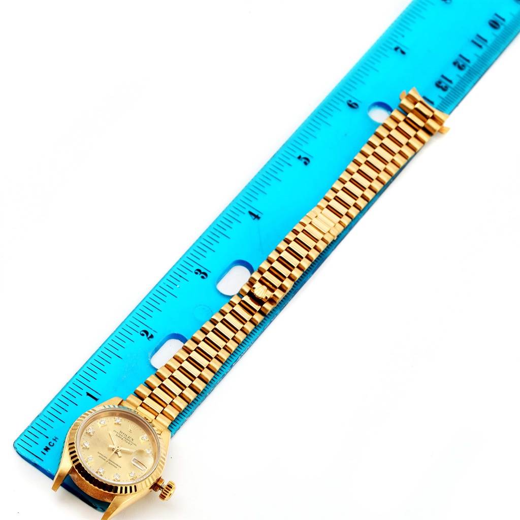 A Rolex President 69178 Women's Yellow Gold Champagne Dial 69178 Women's Yellow Gold Champagne Dial model watch is shown from a top-down angle alongside a blue ruler, highlighting the watch's band and face.