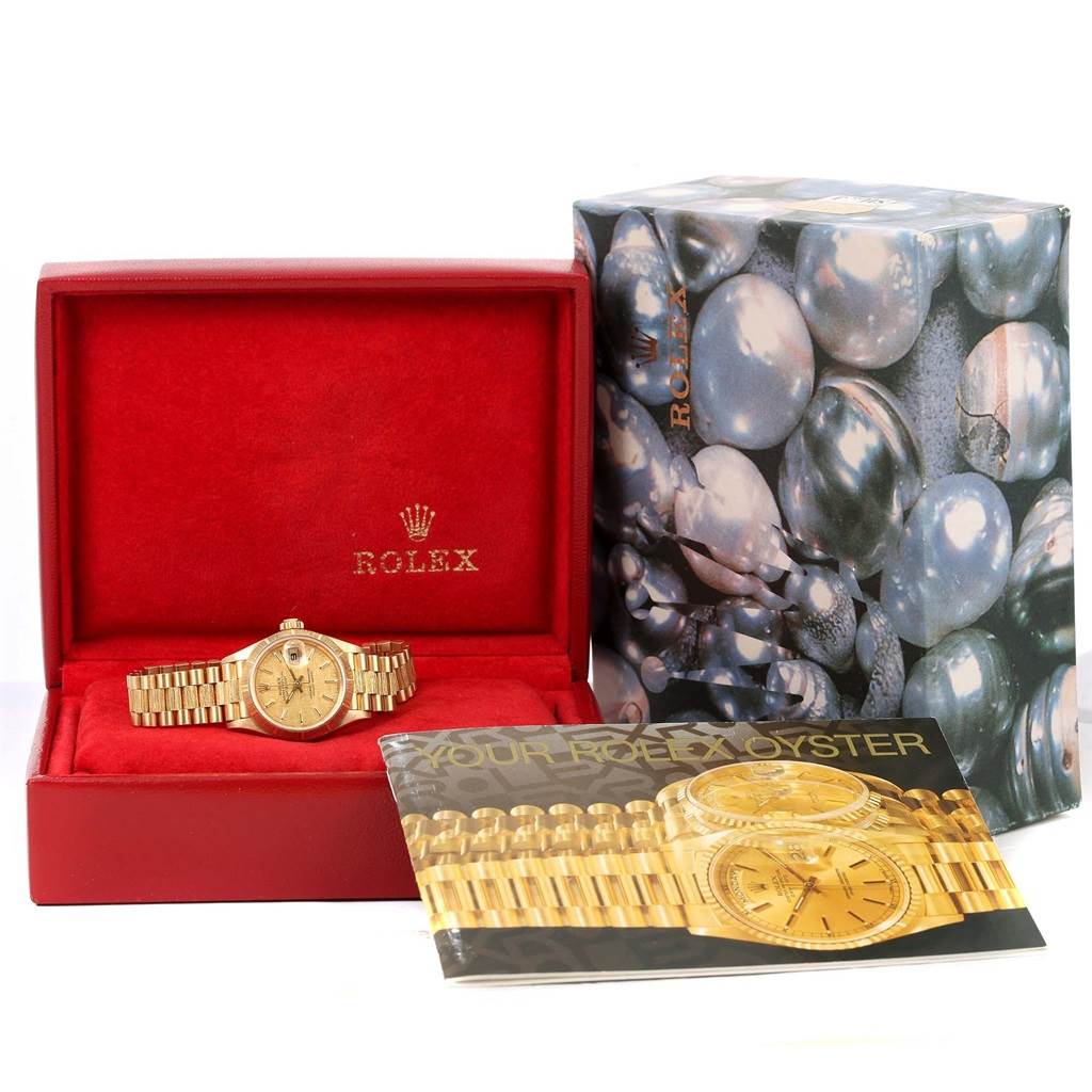 This image shows a Rolex President 69278 Women's Yellow Gold Champagne Dial 69278 Women's Yellow Gold Champagne Dial model watch placed in an open red box with an instruction booklet and decorative outer box beside it.