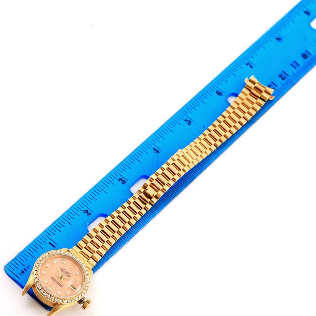 The Rolex President 69138 Women's Yellow Gold Pink Dial 69138 Women's Yellow Gold Pink Dial model watch is shown laid flat with a blue ruler beside it, displaying the band and face.