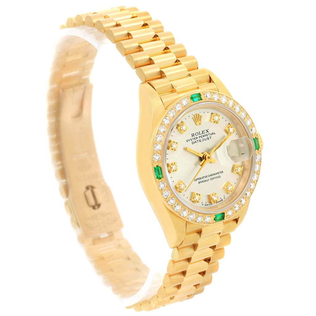 The image shows a side angle view of the Rolex President 69078 Women's Yellow Gold Silver Dial 69078 Women's Yellow Gold Silver Dial watch, displaying its gold bracelet, diamond and emerald bezel, and date window.
