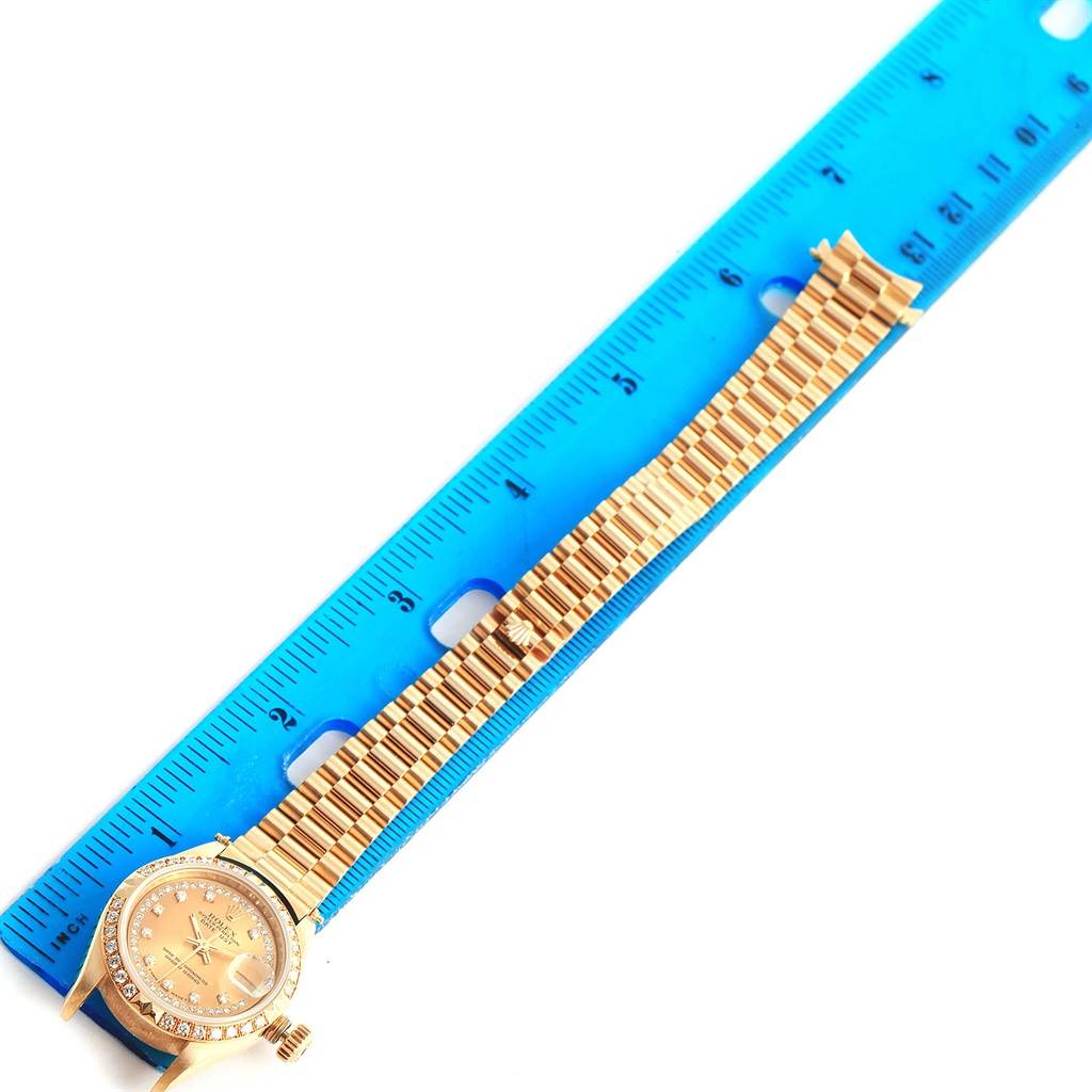 The image shows the Rolex President 69158 Women's Yellow Gold Champagne Dial 69158 Women's Yellow Gold Champagne Dial model watch laid out next to a blue ruler for measurement, capturing the face and bracelet.