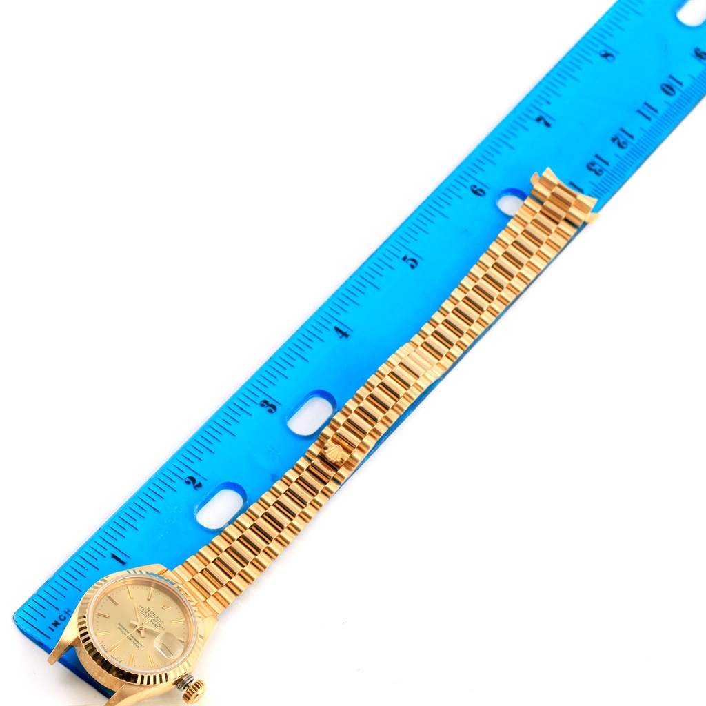 The image shows a gold Rolex President 69178 Women's Yellow Gold Champagne Dial 69178 Women's Yellow Gold Champagne Dial model watch laid flat next to a blue ruler, emphasizing the watch's size and length.