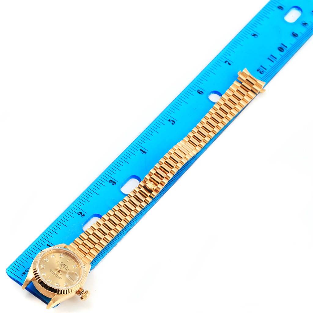 This image shows a Rolex President 69178 Women's Yellow Gold Champagne Dial 69178 Women's Yellow Gold Champagne Dial model watch placed next to a blue ruler, highlighting the band and face from a top-down angle.