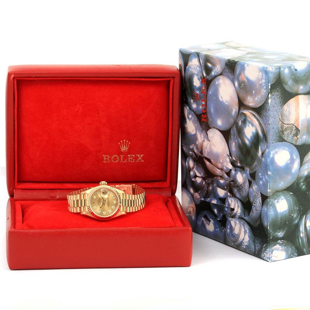 The Rolex President 69178 Women's Yellow Gold Champagne Dial 69178 Women's Yellow Gold Champagne Dial model watch is shown from the front inside its red case, next to its decorative outer box.