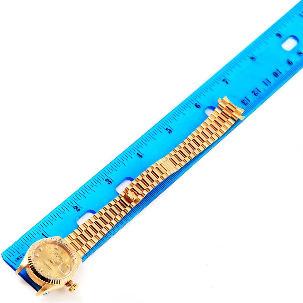 The image shows a Rolex President 69178 Women
s Yellow Gold Champagne Dial 69178 Women
s Yellow Gold Champagne Dial model watch laid next to a blue ruler, displaying the watch face and band.