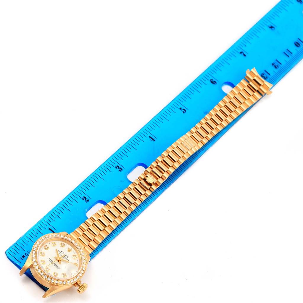 The image shows the face and band of a Rolex President 69138 Women
s Yellow Gold White Dial 69138 Women
s Yellow Gold White Dial model watch, aligned with a blue ruler for measurement.
