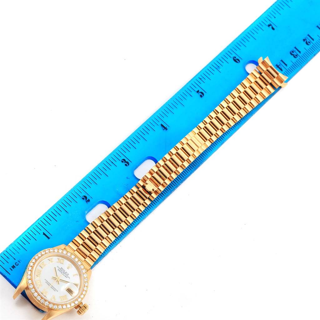 A Rolex President 79178 Women's Yellow Gold Mother of Pearl Dial 79178 Women's Yellow Gold Mother of Pearl Dial model watch is shown laid flat next to a blue ruler, displaying its face and gold bracelet.