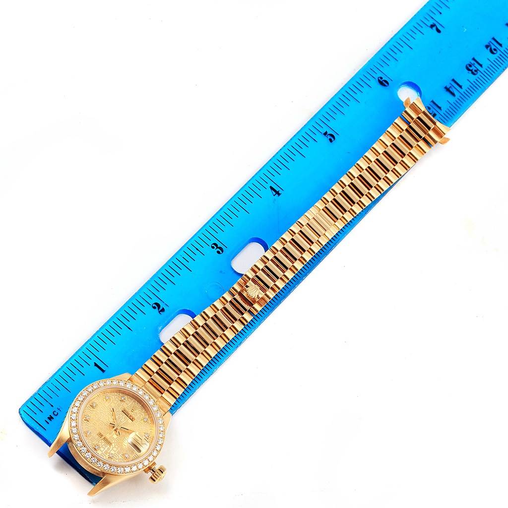 The image shows a Rolex President 69138 Women's Yellow Gold Champagne Dial 69138 Women's Yellow Gold Champagne Dial model watch laid flat with its band extended next to a blue ruler.