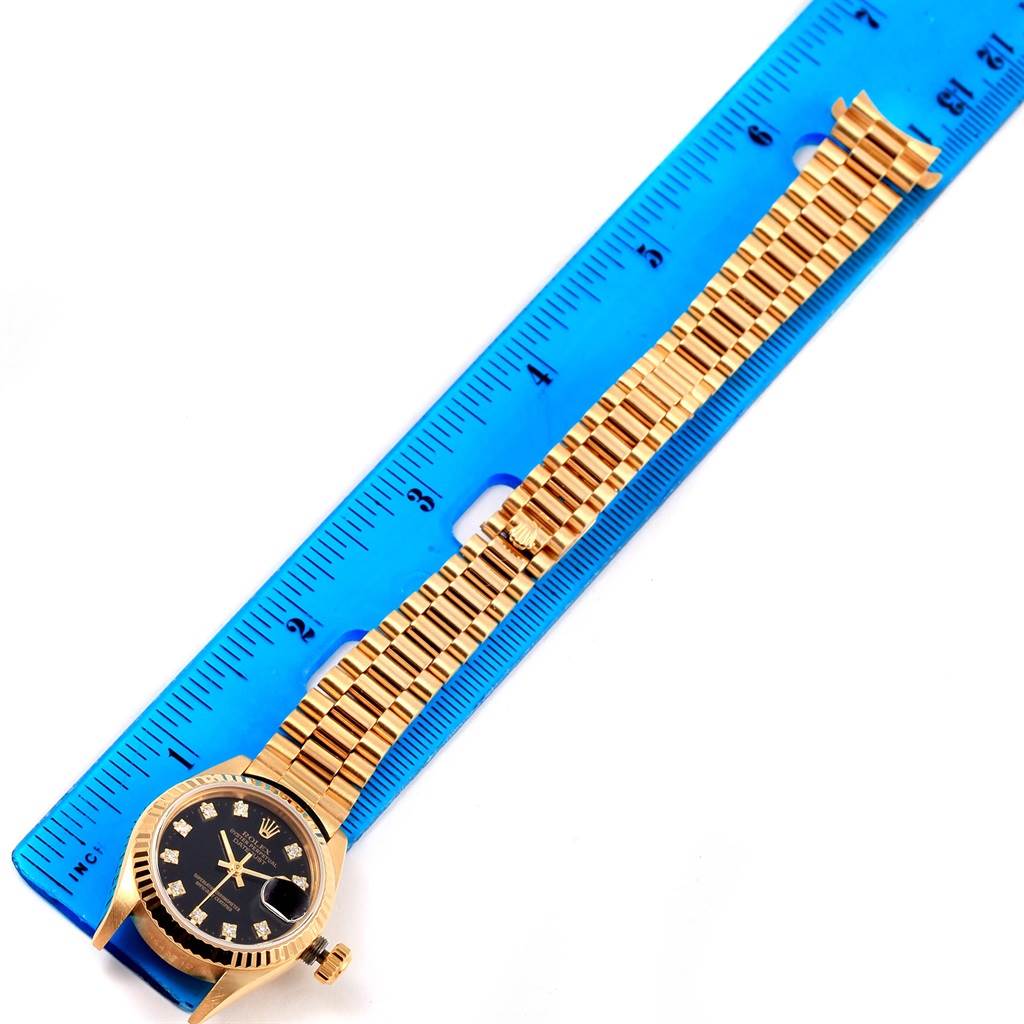 The image shows a gold Rolex President 69178 Women's Yellow Gold Black Dial 69178 Women's Yellow Gold Black Dial watch and its bracelet laid next to a blue ruler for size reference.