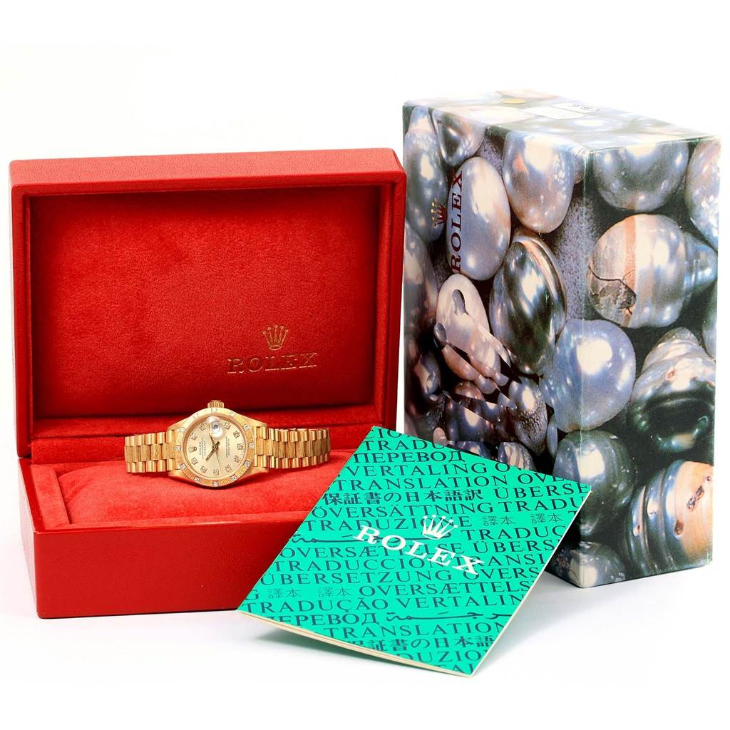 The Rolex President 69288 Women's Yellow Gold Silver Dial 69288 Women's Yellow Gold Silver Dial model watch is displayed in an open red box with its packaging and a booklet alongside.