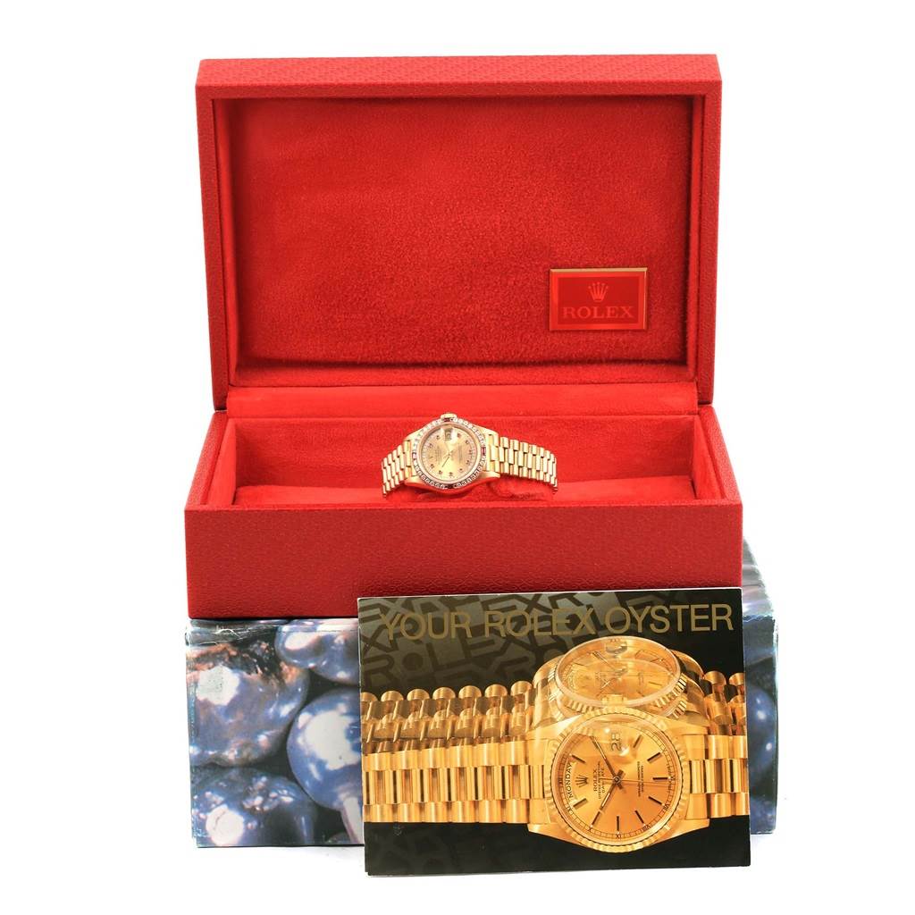 The Rolex President 69178 Women's Yellow Gold Champagne Dial 69178 Women's Yellow Gold Champagne Dial model watch is shown at a straight-on angle inside its red box, accompanied by watch documentation in front.