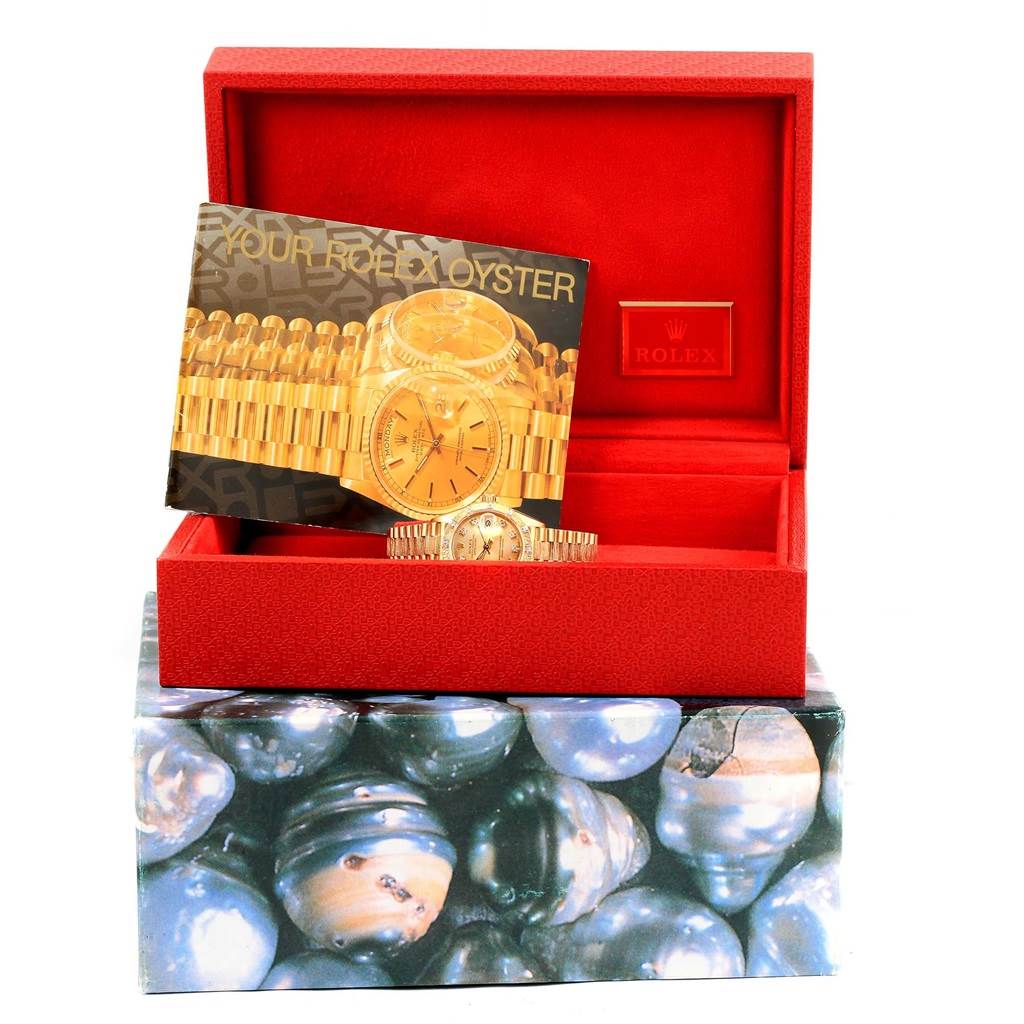 The image shows a Rolex President 69288 Women's Yellow Gold Champagne Dial 69288 Women's Yellow Gold Champagne Dial model watch with its accessories in a red box, including a booklet and a Rolex logo plaque.