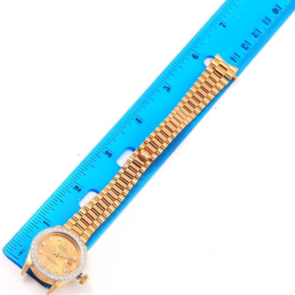 The image shows a Rolex President 6917 Women's Yellow Gold Champagne Dial 6917 Women's Yellow Gold Champagne Dial model watch laid flat next to a blue measuring ruler, highlighting the watch face and bracelet.