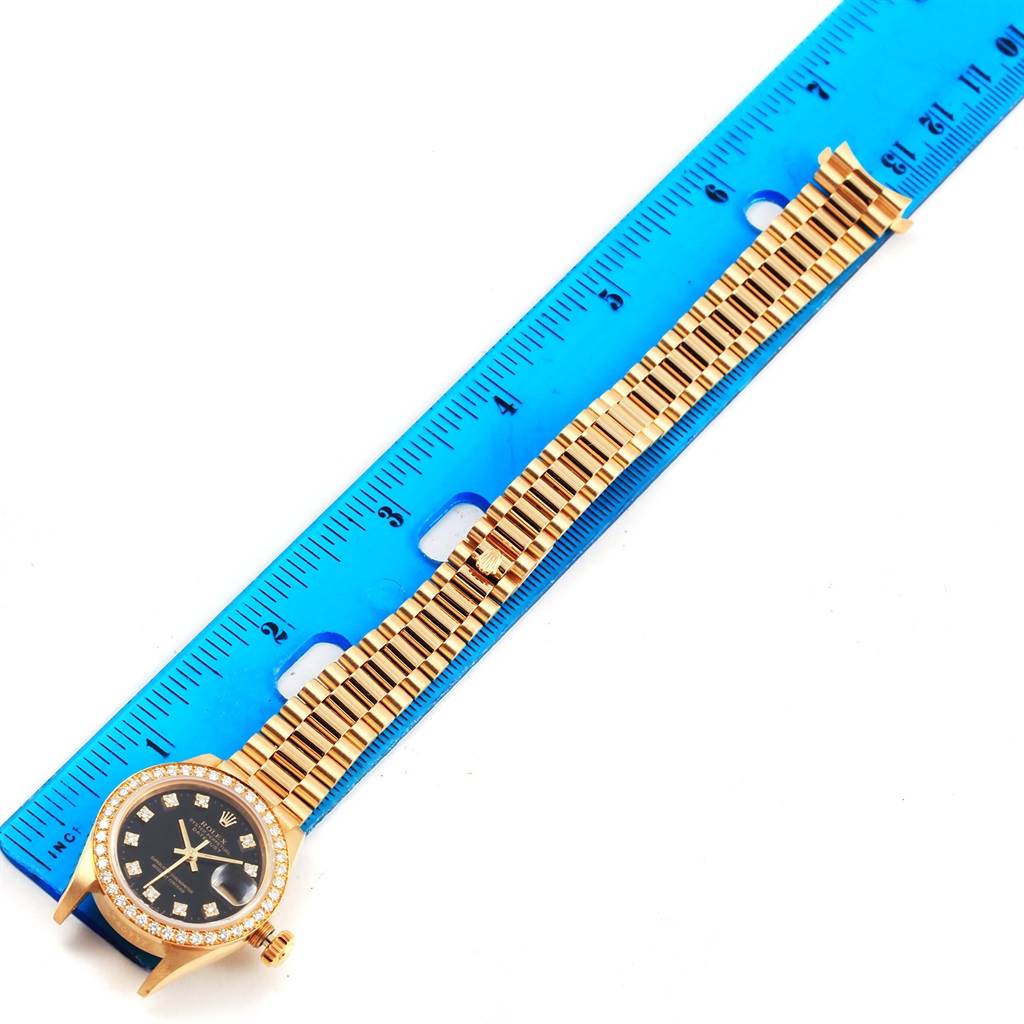 The image shows a top view of a Rolex President 69138 Women's Yellow Gold Black Dial 69138 Women's Yellow Gold Black Dial model watch alongside a blue ruler.