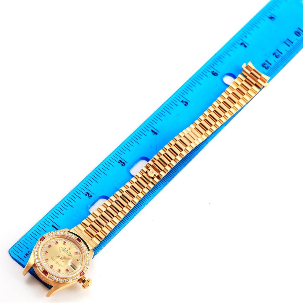The image shows a gold Rolex President 69178 Women's Yellow Gold Champagne Dial 69178 Women's Yellow Gold Champagne Dial model watch with a bracelet-style band next to a blue ruler.