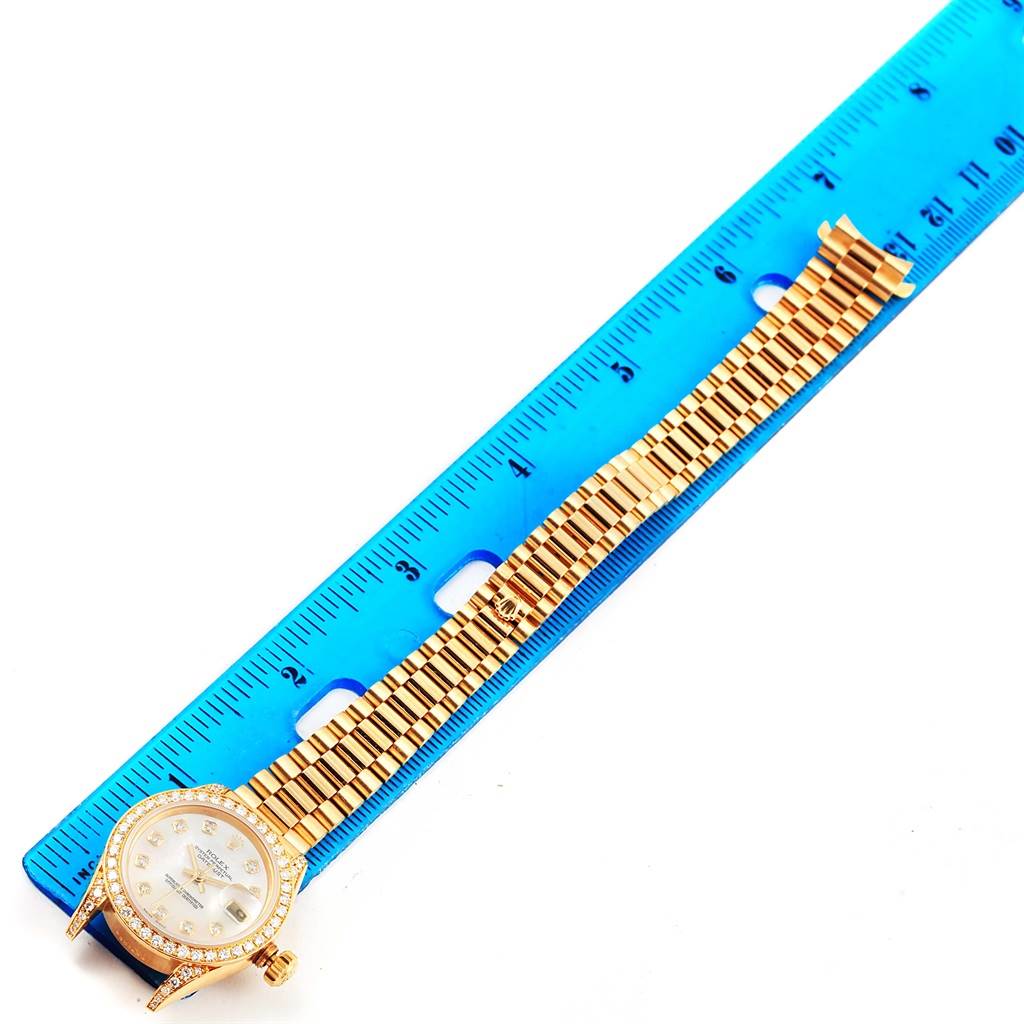 The image shows a Rolex President 79158 Women's Yellow Gold Mother of Pearl Dial 79158 Women's Yellow Gold Mother of Pearl Dial watch lying flat on a blue ruler, displaying the watch face and full metal bracelet.