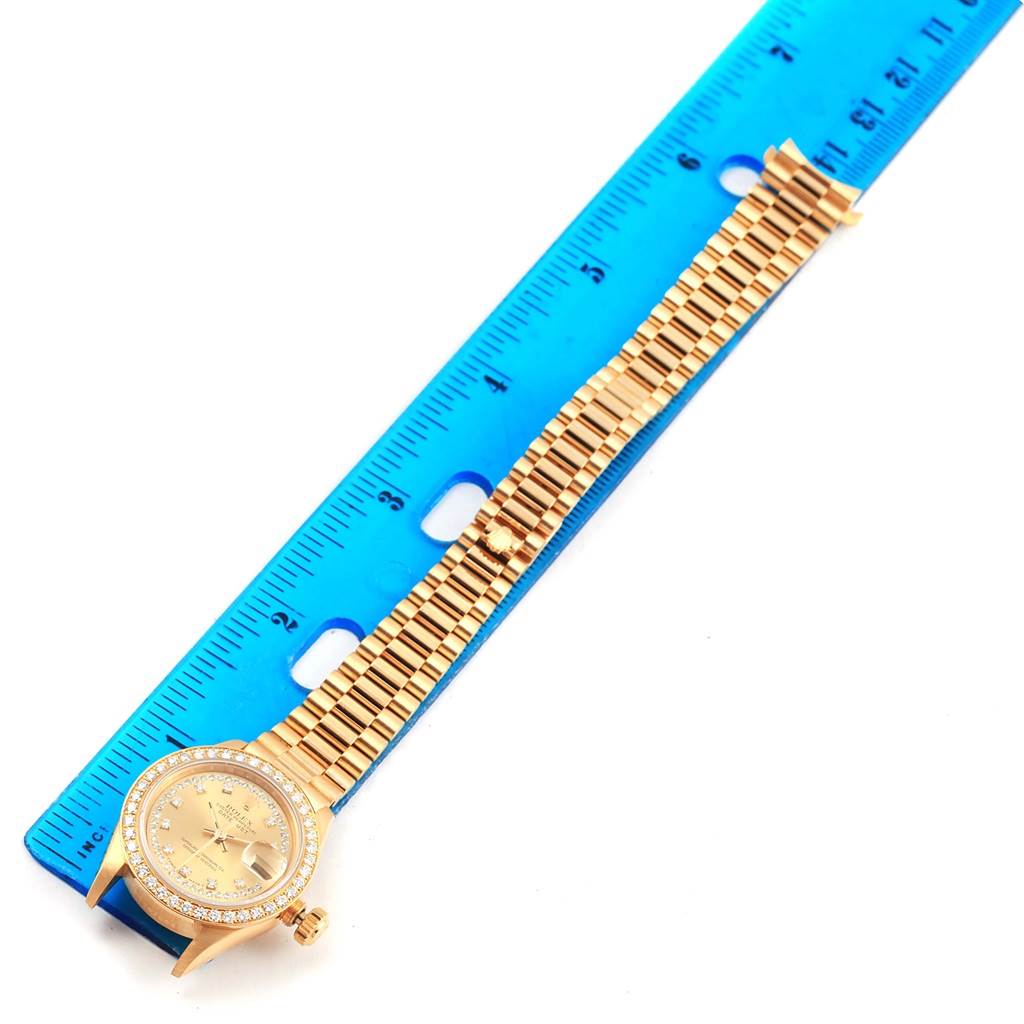 The Rolex President 69138 Women's Yellow Gold Champagne Dial 69138 Women's Yellow Gold Champagne Dial model watch is shown flat with the face, bezel, band, and clasp visible next to a blue ruler.