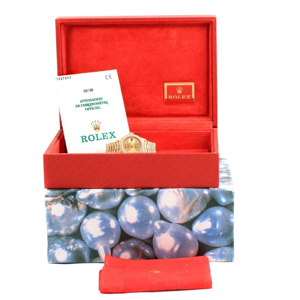 The image shows a Rolex President 69138 Women's Yellow Gold Champagne Dial 69138 Women's Yellow Gold Champagne Dial watch in a red box with documents and the original outer packaging.