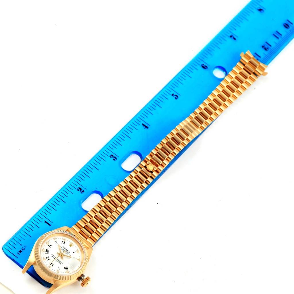 The image shows a Rolex President 69178 Women's Yellow Gold White Dial 69178 Women's Yellow Gold White Dial model watch with a gold bracelet next to a blue ruler for size reference.