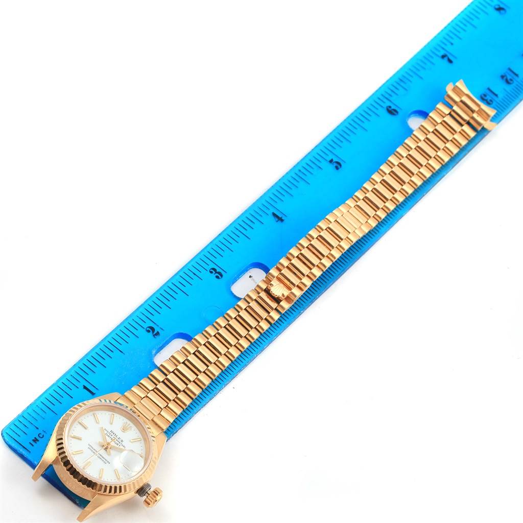 The Rolex President 69178 Women's Yellow Gold White Dial 69178 Women's Yellow Gold White Dial model watch is shown from an overhead angle with its full band and face visible alongside a blue ruler.