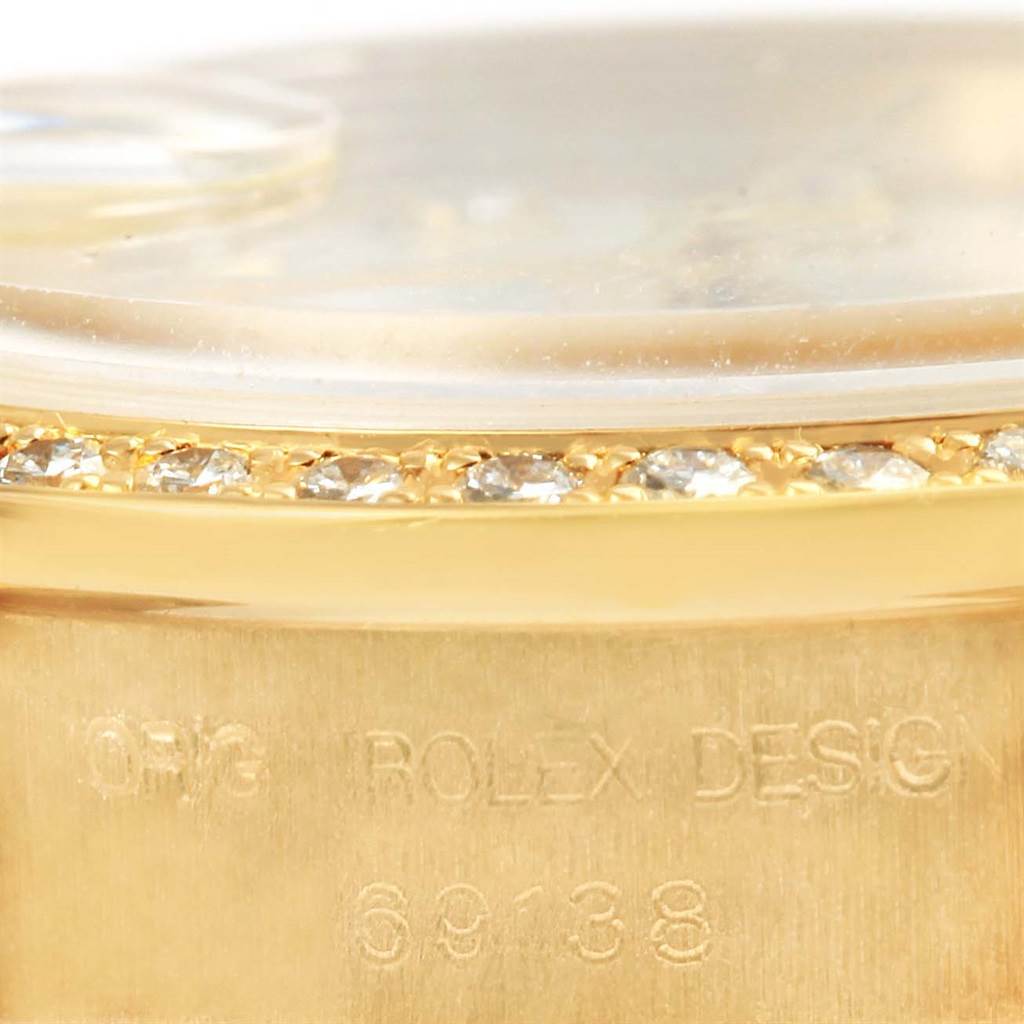The image shows a close-up of the Rolex President 69138 Women's Yellow Gold White Dial 69138 Women's Yellow Gold White Dial model's bezel and case, highlighting its diamond detailing and engraved model number.