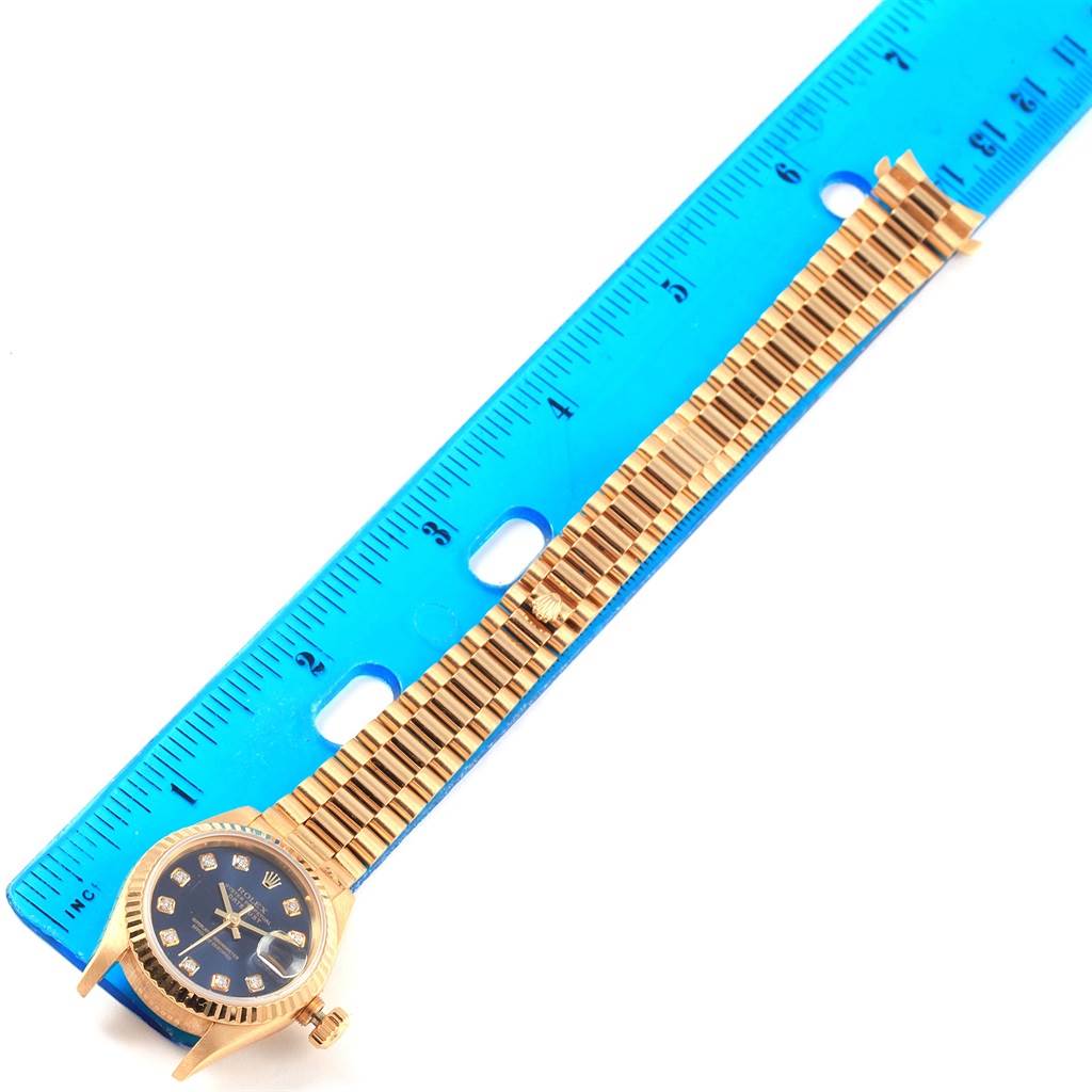 The image shows a gold Rolex President 69178 Women's Yellow Gold Blue Dial 69178 Women's Yellow Gold Blue Dial watch placed alongside a blue ruler for measurement, viewed from above.