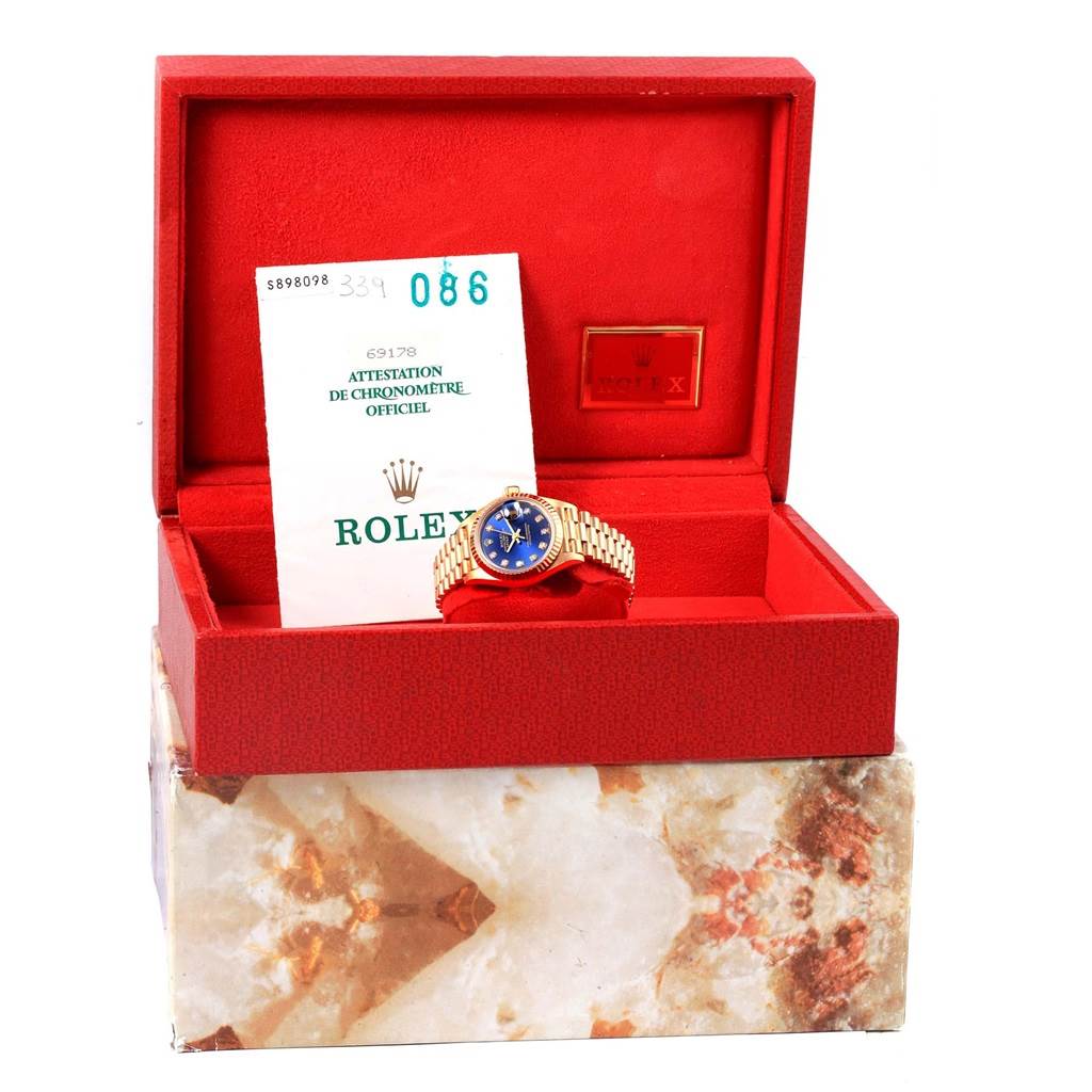 The image shows a Rolex President 69178 Women's Yellow Gold Blue Dial 69178 Women's Yellow Gold Blue Dial watch with a blue dial inside an open red box, accompanied by certification paperwork.