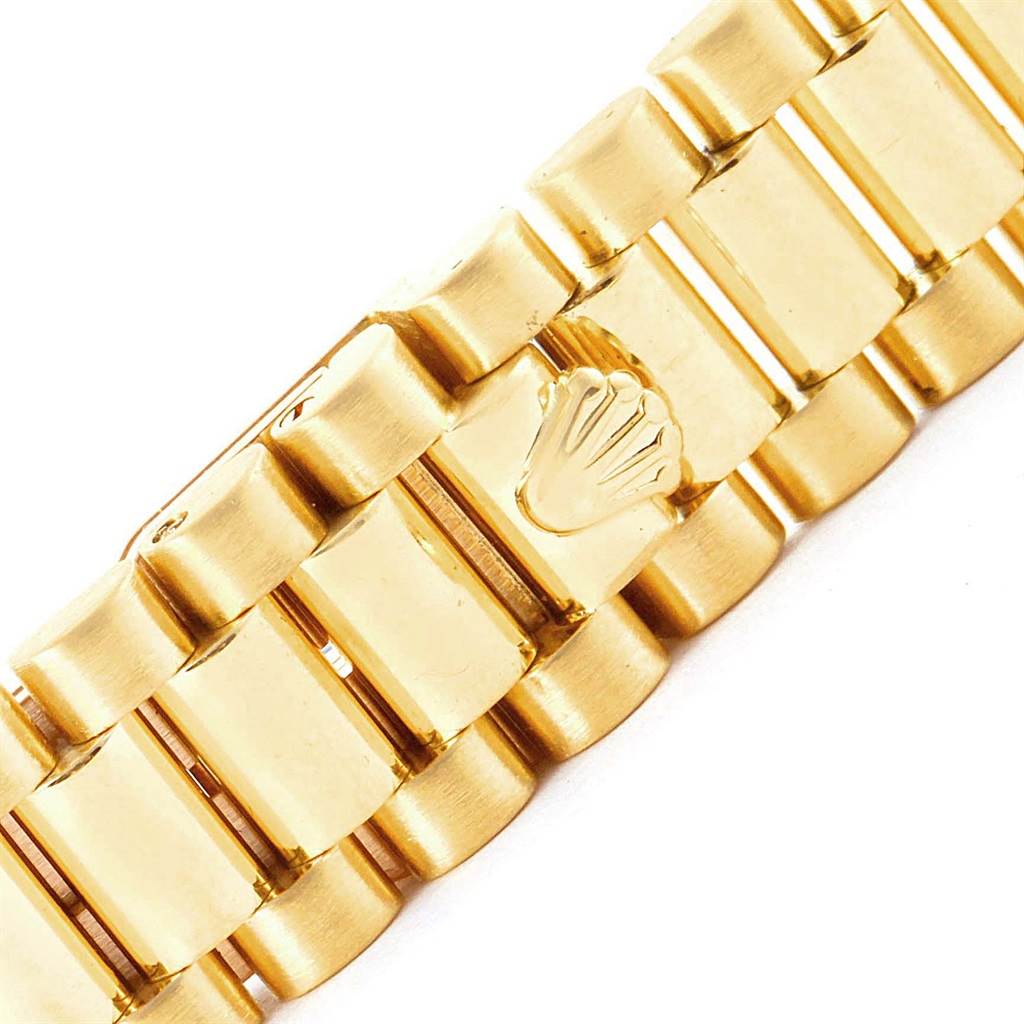 The image displays a close-up of the gold bracelet clasp with the Rolex logo from the President model by Rolex.