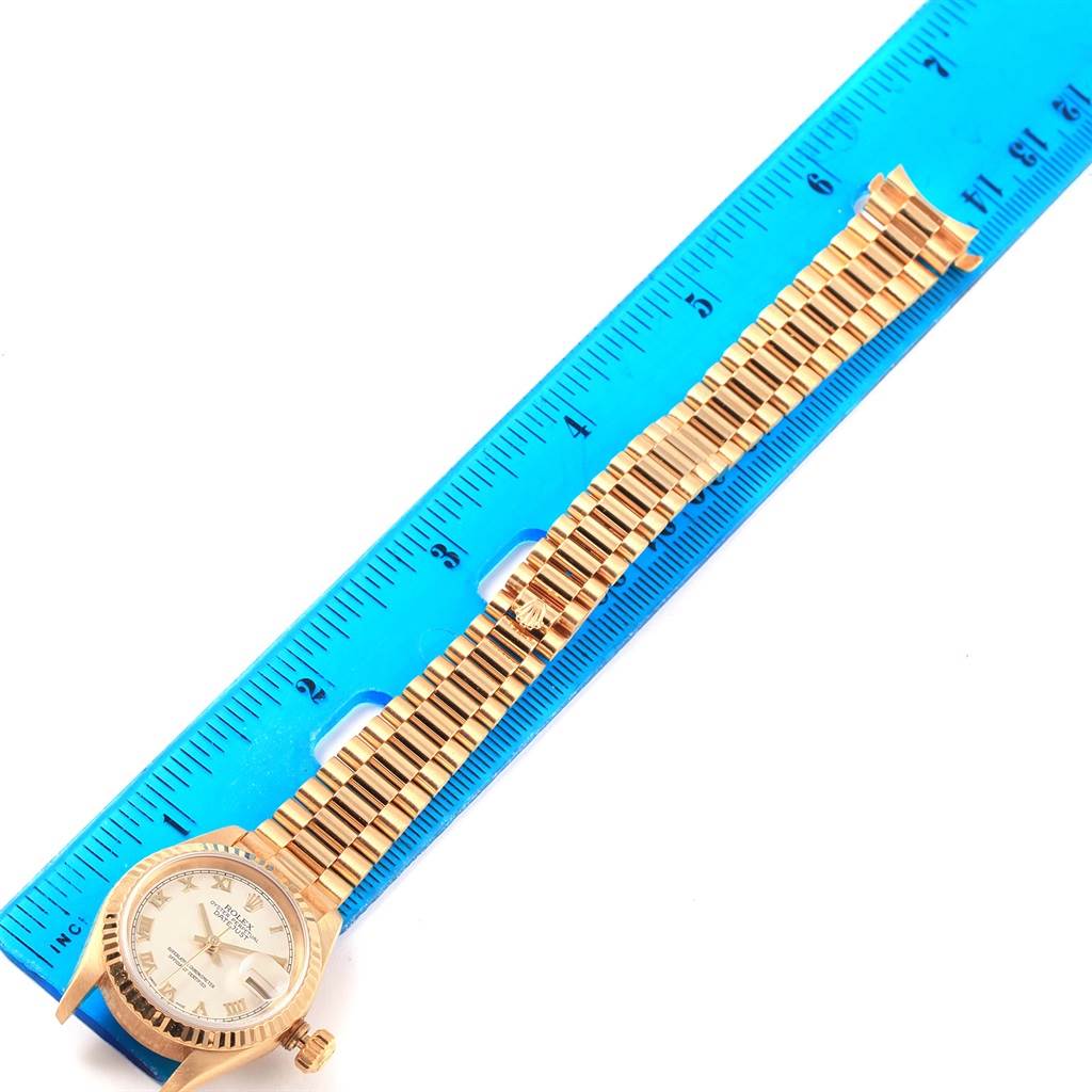 The image shows a President model Rolex watch laid flat next to a ruler, displaying the face and band.