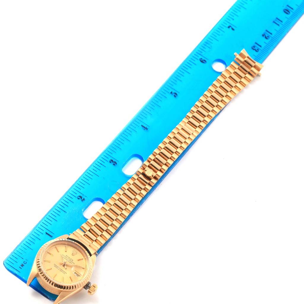 The image shows a Rolex President 6917 Women's Yellow Gold Champagne Dial 6917 Women's Yellow Gold Champagne Dial watch laid flat beside a blue ruler for length measurement.