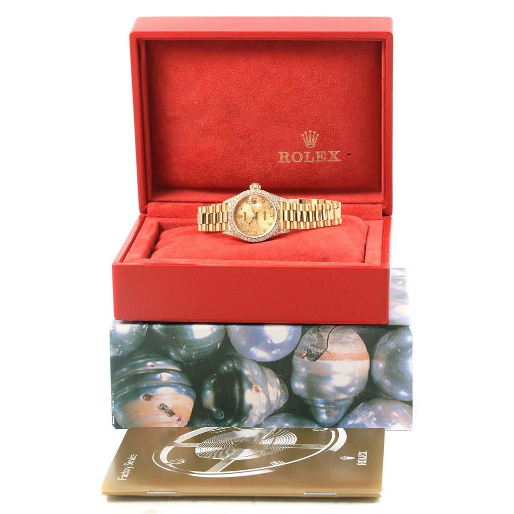 The Rolex President 69158 Women
s Yellow Gold Champagne Dial 69158 Women
s Yellow Gold Champagne Dial model watch is shown from the front, inside an open red box, atop another box with a booklet nearby.
