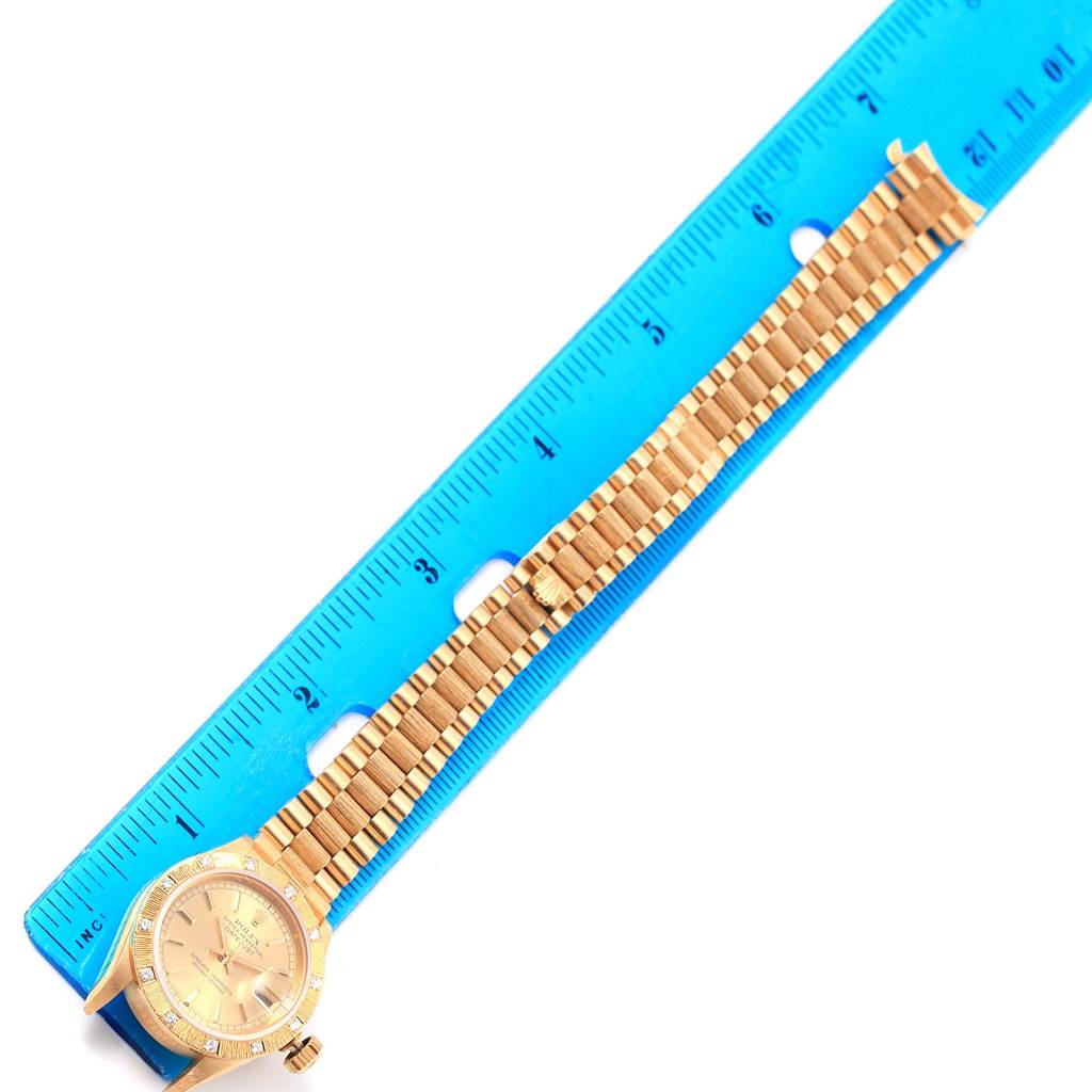 The image shows a Rolex President 69288 Women's Yellow Gold Champagne Dial 69288 Women's Yellow Gold Champagne Dial model watch laying flat alongside a blue ruler, displaying the dial and metal band.