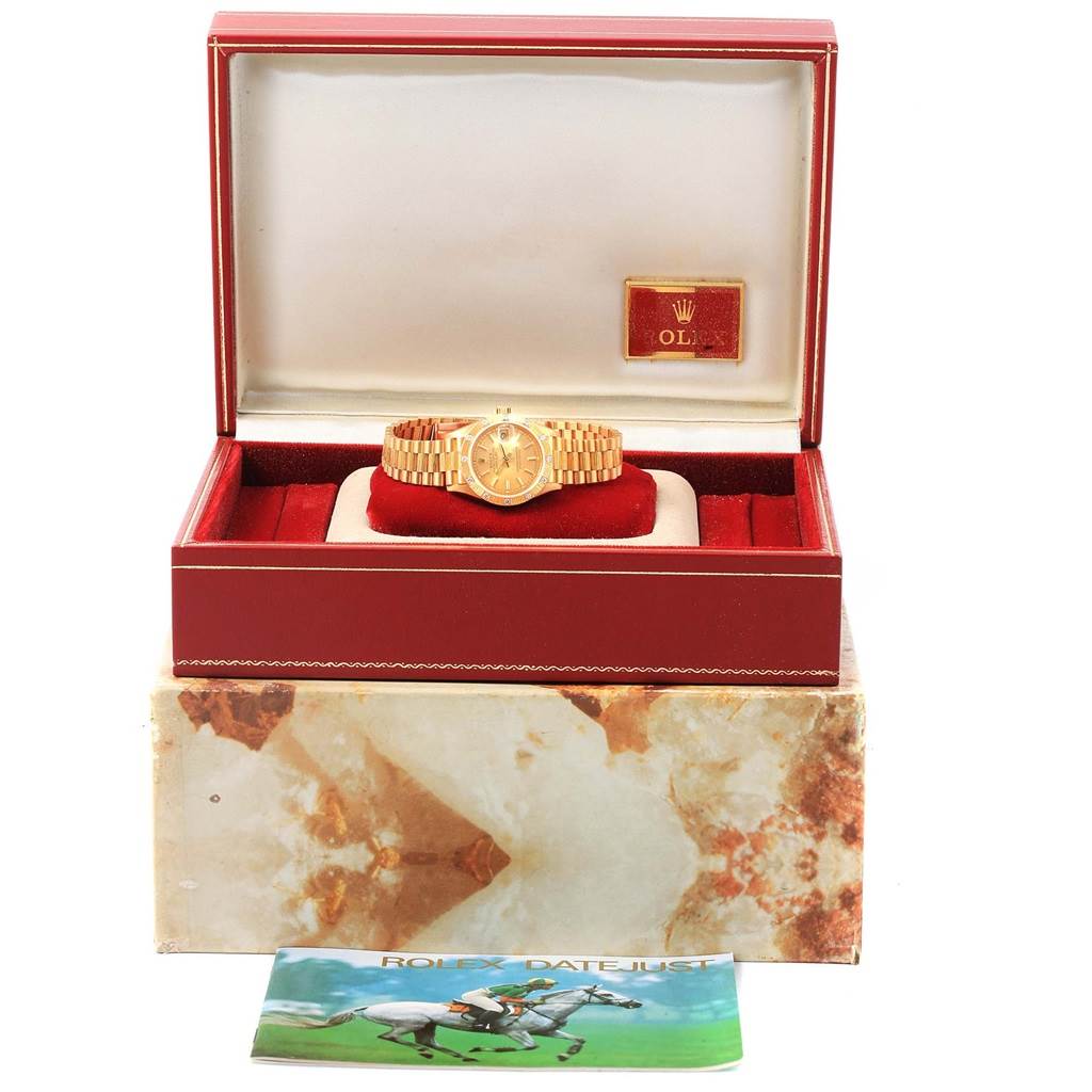 The Rolex President 69288 Women's Yellow Gold Champagne Dial 69288 Women's Yellow Gold Champagne Dial model watch is shown from a frontal angle inside its red and gold box, with its manual displayed in front.