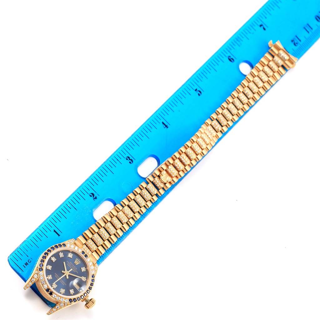 The image shows a Rolex President 69038 Women's Yellow Gold Blue Dial 69038 Women's Yellow Gold Blue Dial model watch and its full band laid flat next to a blue ruler.