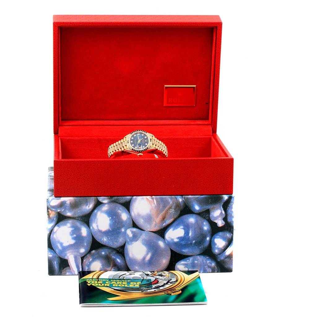 The image shows a Rolex President 69038 Women's Yellow Gold Blue Dial 69038 Women's Yellow Gold Blue Dial model watch inside an open red case, with an information booklet in front.