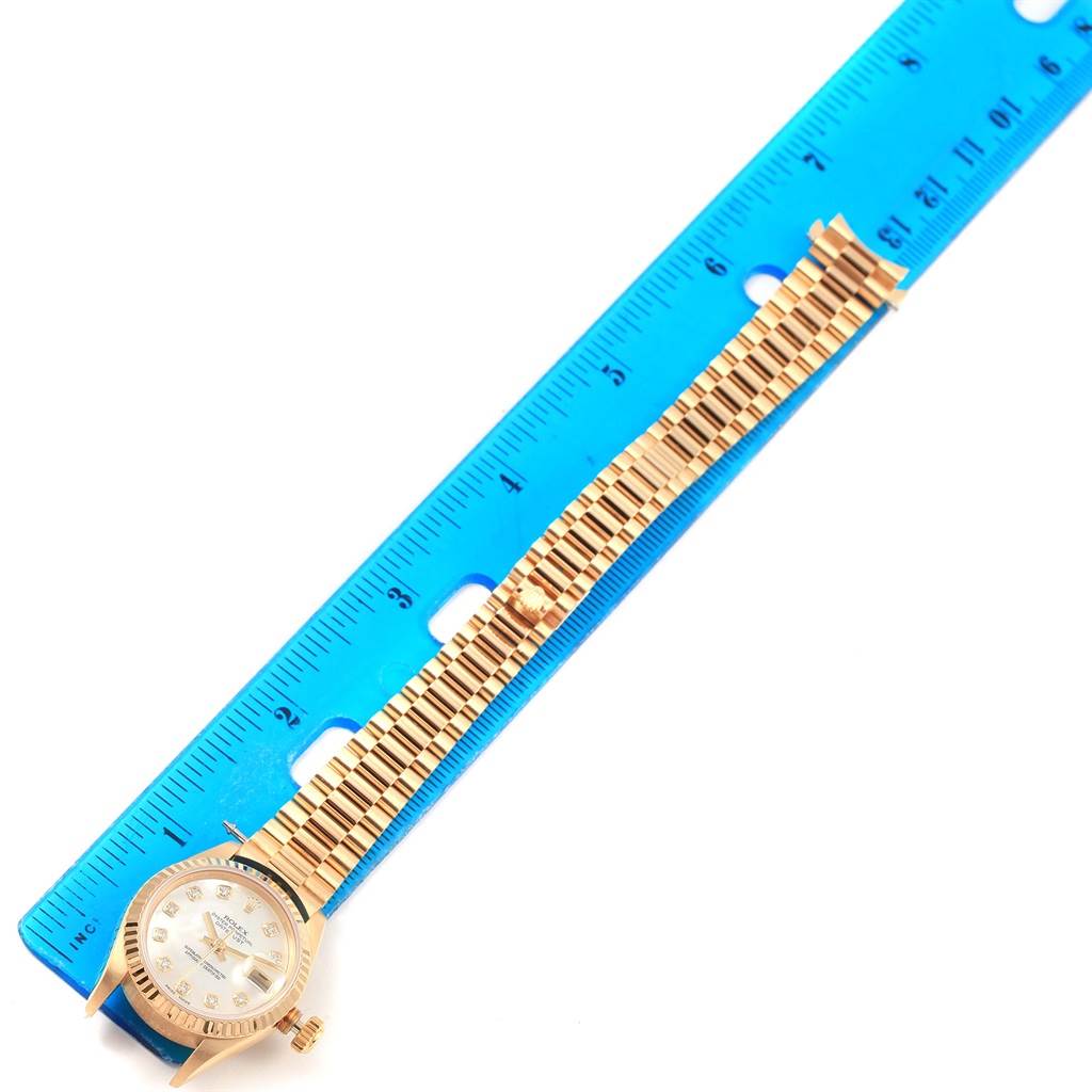 The image shows a Rolex President 69178 Women's Yellow Gold Mother of Pearl Dial 69178 Women's Yellow Gold Mother of Pearl Dial model watch positioned next to a blue ruler, displaying the watch's dial and bracelet.