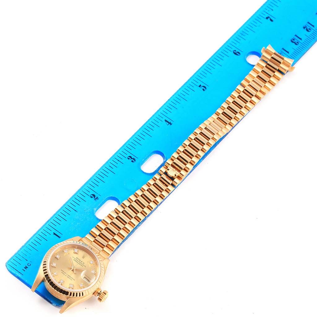 The Rolex President 69178 Women's Yellow Gold Champagne Dial 69178 Women's Yellow Gold Champagne Dial model watch is shown with a gold dial, bracelet, and a blue ruler for measurement.